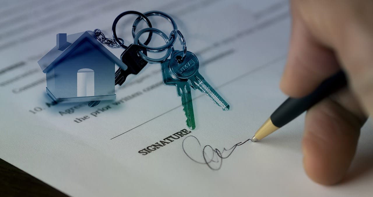 A hand signing a purchase contract beside house keys